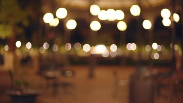 夜晚城市街道上的空椅子和空桌子的背景板不清晰 Bokeh拍摄的城市公园与咖啡馆风格的桌子和街灯 — 图库视频影像