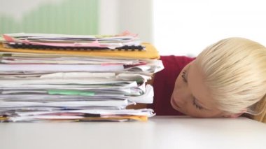 Kafası masanın üzerinde, büyük kağıt yığınının yanında duran bir iş kadını.
