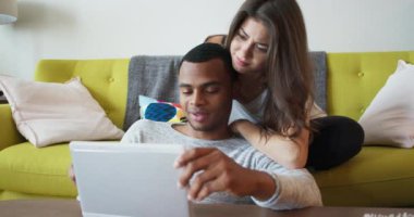 Genç milenyum çifti, tatillerini birlikte oturma odasında geçirmek için tablet bilgisayar kullanıyor. Çevrimiçi cihaz kullanan Afrikalı Amerikalı ve Kafkasyalı sevgili. 4k Yavaş çekim el bilgisayarı