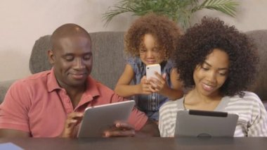 Cep telefonu ve tablet kullanan Afrikalı Amerikalı bir aile.