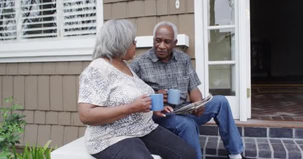 Senior Μαύρο Ζευγάρι Κάθεται Στη Βεράντα Διαβάζοντας Εφημερίδα — Αρχείο Βίντεο