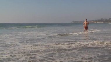 Genç adam okyanus sahilinde koşuyor.