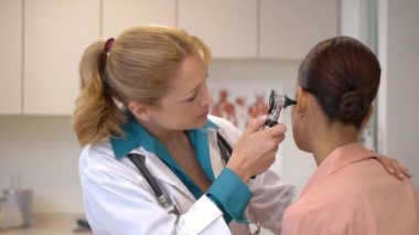 Kadın doktor hastanın kulağına bakıyor.