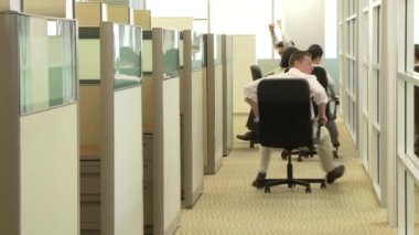 Genç iş arkadaşları ofiste sandalyelerle yarışıyorlar.