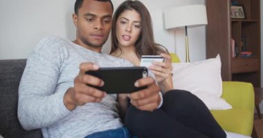 Afrika kökenli Amerikalı ve Kafkasyalı çift, kredi kartı ve akıllı telefon kullanarak online alışveriş yapıyorlar. Milenyum yeni evlileri balayı tatili için rezervasyon yaptırıyor. 4k ağır çekim el bilgisayarı