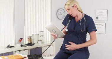 Hamile hemşire ofiste telefonla konuşuyor.