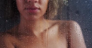 Çıplak siyah kadın bulanık camın arkasında duruyor.