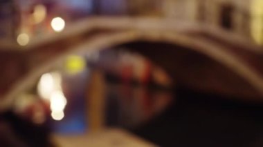 İtalya, Venedik 'te dar bir kanalın üzerindeki kemerli yapının bulanık arka plan plakası. Venedik köprüsünün altından yansıyan güzel ışıklar. 4k