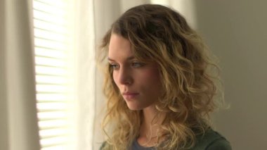 Sarışın, kıvırcık saçlı kadın pencerede bekliyor.