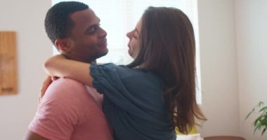 Mutlu Afrikalı Amerikalı erkek arkadaş öpüşürken gülümseyen kız arkadaşını tutuyor. Yeni dairede kucaklaşan ve öpüşen çekici genç bir çift. 4k Yavaş çekim el bilgisayarı