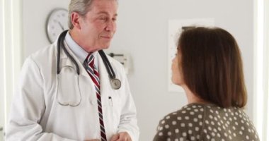 Doktor ofiste yaşlı bir kadınla konuşuyor.