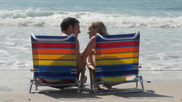 若いですカップル座っていますラウンジチェアによって海とキス — ストック動画