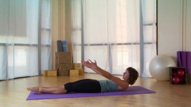 Genç bir kadın paspasın üzerinde pilate hareketi yapıyor.