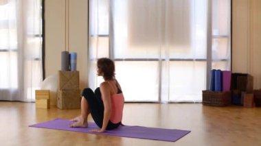 Genç bir kadın paspasın üzerinde pilate hareketi yapıyor.