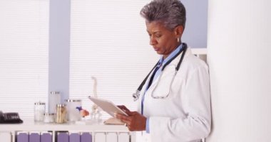 Ciddi siyah kıdemli doktor ofisinde tablet üzerinde çalışan