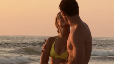 Gün batımında sahilde öpüşen genç çiftin yakın çekimi.