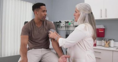 Kıdemli bayan doktor, genç siyahi erkeklerin tansiyonunu monitör ve stetoskopla ölçüyor. Afro-Amerikalı genç bir hastanın kan basıncını ölçen Kafkas bir doktor.