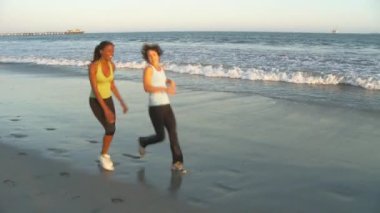 Kumsalda koşunun sonunda soluklanan iki genç kadın.