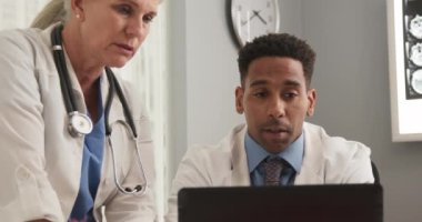 Genç Afro-Amerikan doktorların, üst düzey meslektaşlarıyla birlikte ofis içinde dizüstü bilgisayar kullanmalarına yakın çekim. İki tıp doktoru birlikte çalışıyor ve defter bilgisayarı kullanıyorlar.