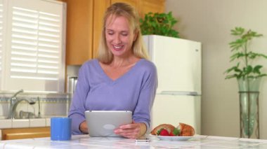 Tablet kullanan ve kahve içen olgun bir kadın.