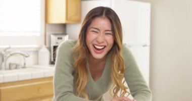 Japon kadın kameraya bakıyor ve mutfakta otururken konuşuyor.