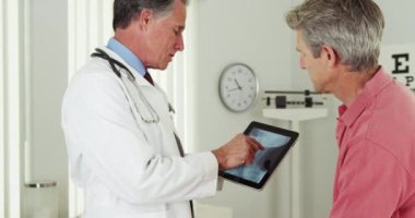 Doktor olgun bir hastayla tabletteki röntgenini konuşuyor.