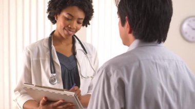 Afrikalı Amerikalı doktor hastanın tıbbi geçmişini dolduruyor.