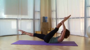 Genç bir kadın paspasın üzerinde pilate hareketi yapıyor.