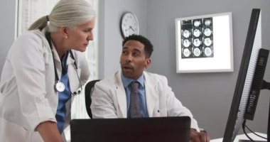 Bilgisayar monitörüne bakıp notları karşılaştıran iki doktor. Genç siyahi doktor, beyaz kıdemli meslektaşıyla görüşürken dizüstü bilgisayarda yazı yazıyor.