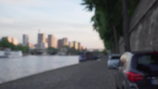パリのセーヌ川を挟んで都市の都市のシーンをぼやけている 遠くに超高層ビルが建ち並ぶ川沿いに停まっている車 — ストック動画