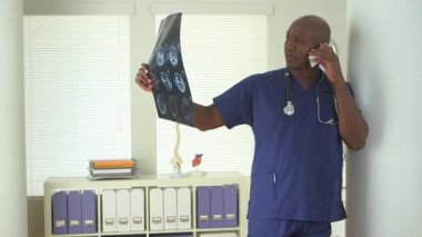 Siyahi doktor telefonda konuşuyor ve CT taramalarını inceliyor.