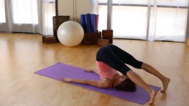 Genç bir kadın paspasın üzerinde pilate hareketi yapıyor.