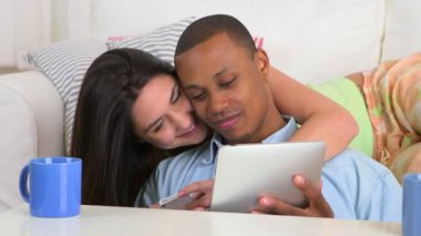 Mutlu Afro-Amerikalı ve Kafkasyalı çift tablet bilgisayar ve akıllı telefon kullanıyor.