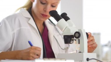 Mikroskop kullanan ve not yazan bir tıp araştırmacısı.