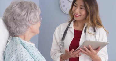 Yatakta yaşlı kadın konuşurken tablet bilgisayar kullanarak Asya hekim