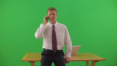 İş adamı masanın kenarında oturuyor ve cep telefonuyla konuşuyor.