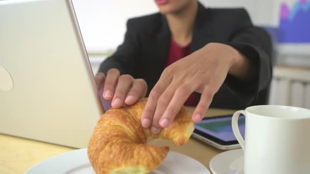 アフリカ系アメリカ人のビジネス女性がデスクでクロワッサンを食べる — ストック動画