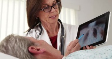 Yatakta yatan kıdemli hastayla konuşan profesyonel bir doktor.