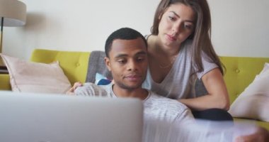 Afro-Amerikalı ve Kafkasyalı çift dizüstü bilgisayarla faturalarını ödüyor. Milenyum yeni evlileri oturma odasında oturup evrakları gözden geçiriyorlar. 4k Yavaş çekim el bilgisayarı
