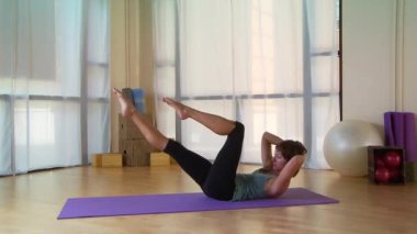 Genç bir kadın paspasın üzerinde pilate hareketi yapıyor.