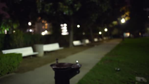 ベンチで夜の空公園のぼやけたビデオ背景プレート 空の道と組成物のための都市公園内の飲料噴水のビデオ背景を強調した — ストック動画