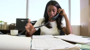 Masada çalışan genç bir iş kadını ve ofiste telefonlara bakan.