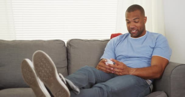 テキスト メッセージのソファの上に座って黒人男性 — ストック動画