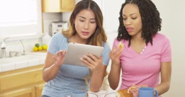 Siyah ve Japon arkadaşlar kahvaltı yapıyorlar ve tablet bilgisayar kullanıyorlar.