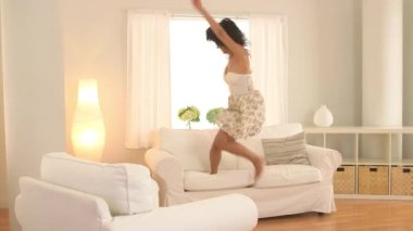 Asyalı kadın kanepede zıplıyor ve oturma odasında dans ediyor.