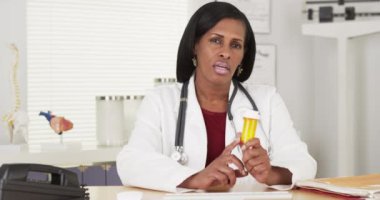 Kıdemli siyahi doktor kameraya ilaç şişesinden bahsediyor.