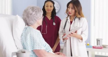 Japon Doktor ve siyah hemşire yaşlı kadın hasta hastane yatağında konuşuyor