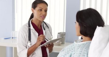 Afrikalı Amerikalı doktor yatakta İspanyol bir hastayla konuşuyor.