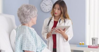 Japon doktor hastane yatağında yaşlı bir kadınla konuşuyor.