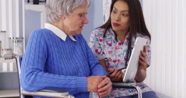 Neşeli Meksikalı bakıcı tabletli yaşlı bir hastayla konuşuyor.